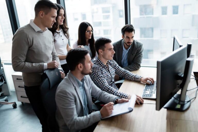 Un groupe de jeunes professionnels réunis autour d'un bureau, regardant ensemble l'écran d'un ordinateur dans un environnement de bureau.