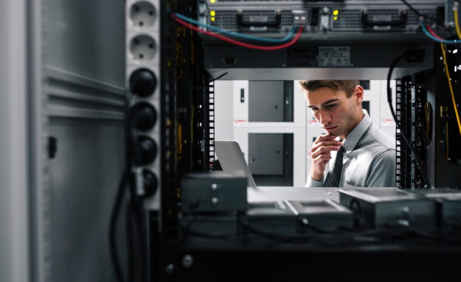 Profesional de TI inspeccionando un rack de servidores, mirando una computadora portátil en un centro de datos.