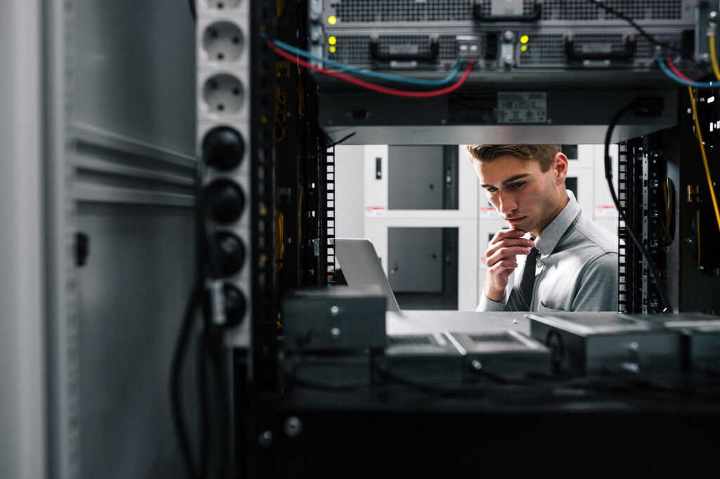 IT professional inspecting a server rack, looking at a laptop in a data center.