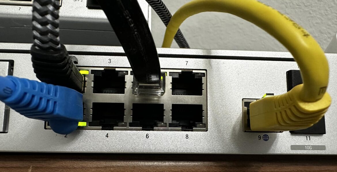 Netzwerk-Switch mit blauem und gelbem Ethernet-Kabel, die in Ports eingesteckt sind, zeigt Portnummern und verwendete Kabel.