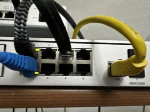 Conmutador de red con cables Ethernet azules y amarillos enchufados en los puertos, mostrando los números de los puertos y los cables en uso.