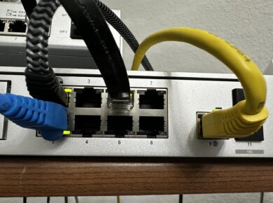 A network switch with blue and yellow Ethernet cables plugged into the ports, showing the port numbers and which cables are in use.