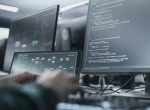 Desarrolladores de software programando en escritorios con múltiples monitores que muestran código y paneles.