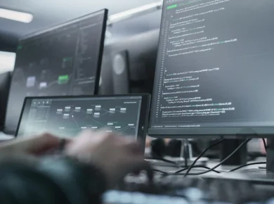 Software developers coding at desks with multiple monitors displaying code and dashboards.