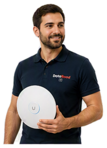 A bearded man in a navy polo shirt, holding a round white wireless device with a blue ring and a 'U' button, wearing a polo shirt with the DotaRoad logo.