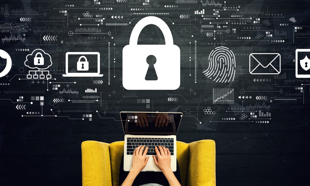 Personne tapant sur un ordinateur portable sur une chaise jaune, avec un grand cadenas et des icônes de sécurité numérique flottant au-dessus, illustrant la cybersécurité.