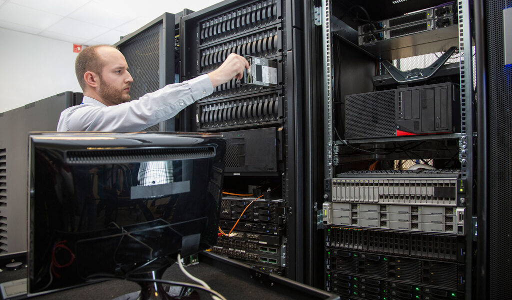 An IT technician in a data centre inserting a hard drive into a server