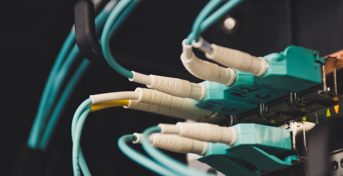 Nahaufnahme von türkisfarbenen Ethernet-Kabeln, die in ein Netzwerk-Patchpanel in einem Server-Rack eingesteckt sind, schwach beleuchtet.