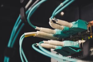 Primer plano de cables Ethernet verde azulado enchufados en un panel de conexiones de red en un bastidor de servidores, tenuemente iluminado.