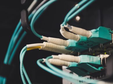 Close-up of teal Ethernet cables plugged into a network patch panel in a server rack, dimly lit.