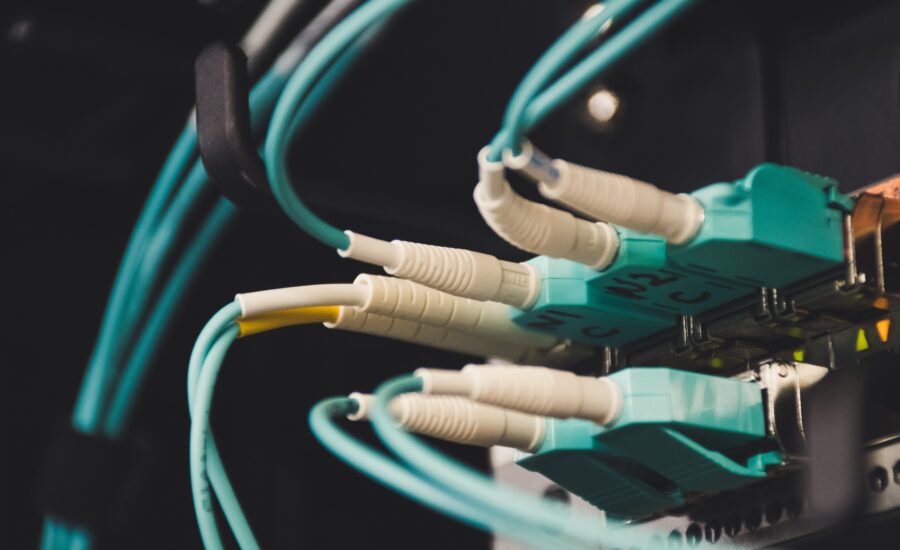 Primer plano de cables Ethernet verde azulado enchufados en un panel de conexiones de red en un bastidor de servidores, tenuemente iluminado.