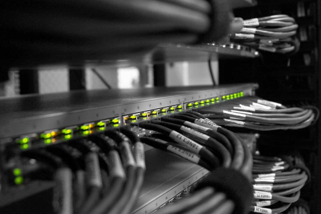 Network rack with a row of illuminated green LEDs on a switch and bundled Ethernet cables labeled and organized in a server cabinet