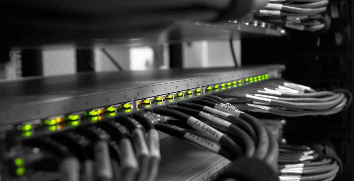 A network rack with a row of illuminated green LEDs on a switch and bundled Ethernet cables, labelled and organised inside a server cabinet