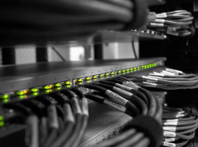 Bastidor de rede com switch de LEDs verdes e cabos de rede organizados e etiquetados