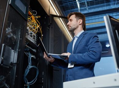 IT professional in a blue suit inspecting server racks with a laptop in a data center
