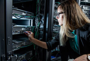 optimiser-les-actifs-materiels-et-logiciels - DataRoad Une technicienne informatique dans un centre de données branche un câble réseau sur un serveur monté en rack.