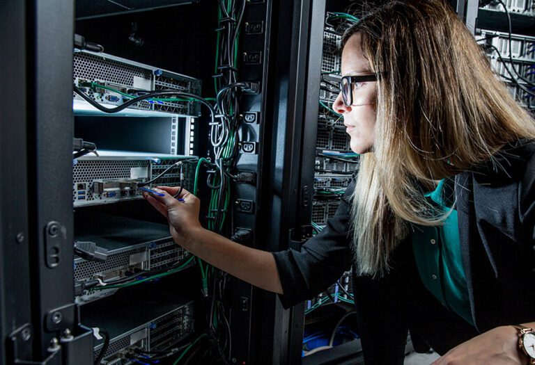 Female IT technician in a data center plugs a network cable into a rack-mounted server.