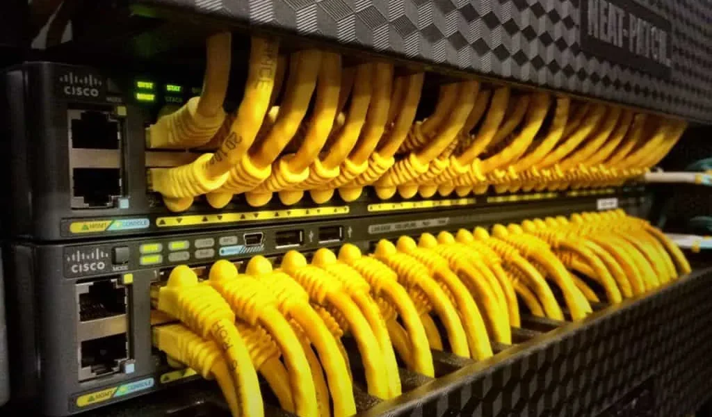 A row of Cisco network switches with numerous yellow Ethernet cables connected to them.